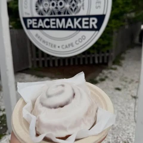 A frosted cinnamon roll held up in front of the Peacemaker roadside sign