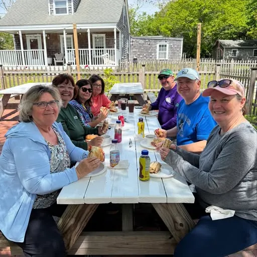 Customers around the picnic table on the patio with sandwiches and iced drinks