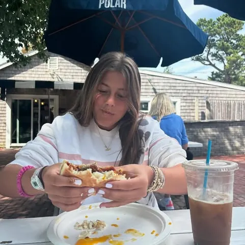 A customer at a patio table under an umbrella with a breakfast sandwich and an iced coffee